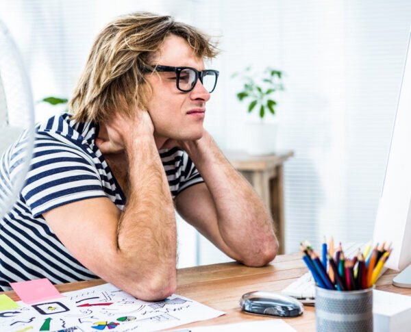 Focused artist reviewing caricature sketches” – A caricature artist deep in thought as he reviews his work on a computer, with drawing tools spread out on the desk.